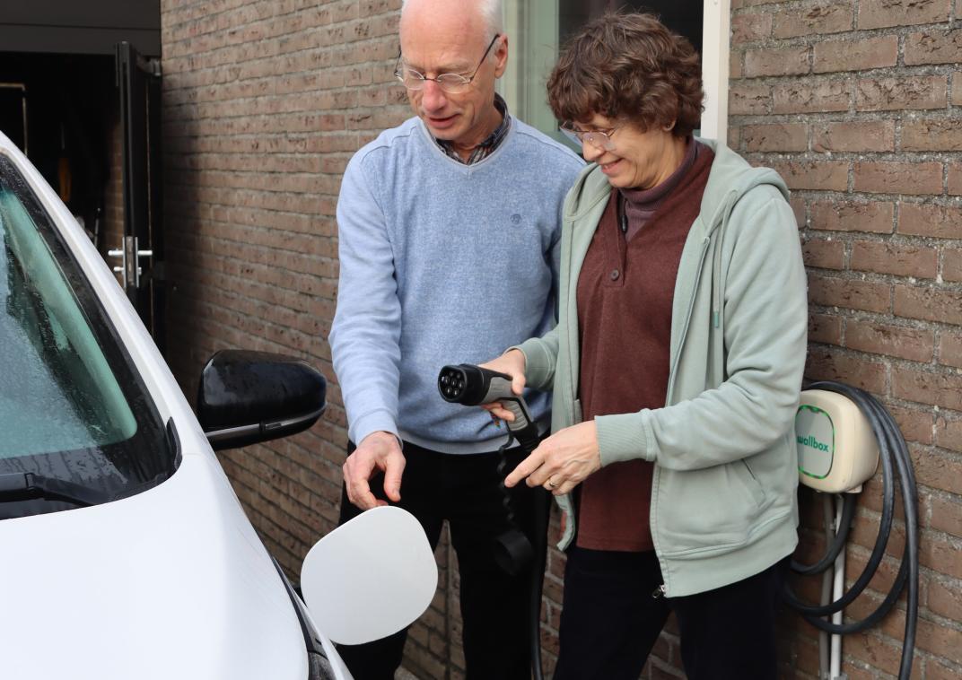 Man en vrouw bij hun elektrische laadpaal aan hun woning