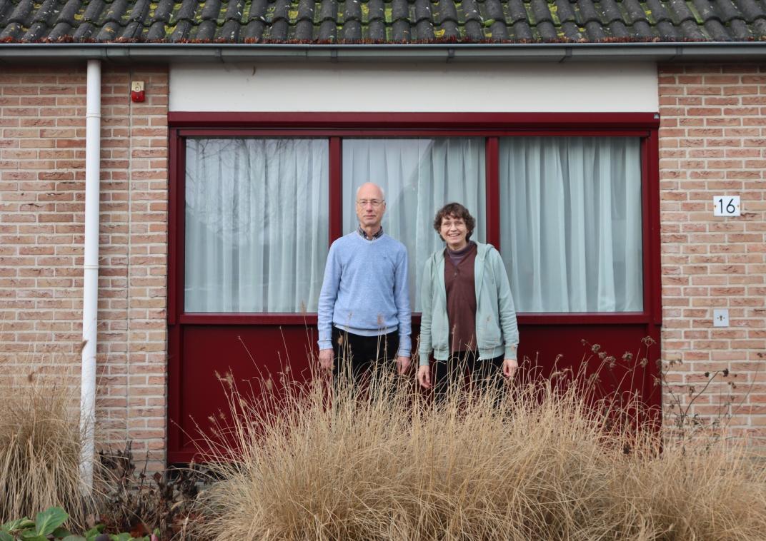 Een man en een vrouw staan buiten bij hun huis met duidelijk de zonnepanelen in beeld. 