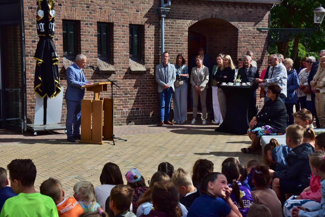 Foto van opening, kinderen zitten op de grond publiek staat tijdens toespraak wethouder